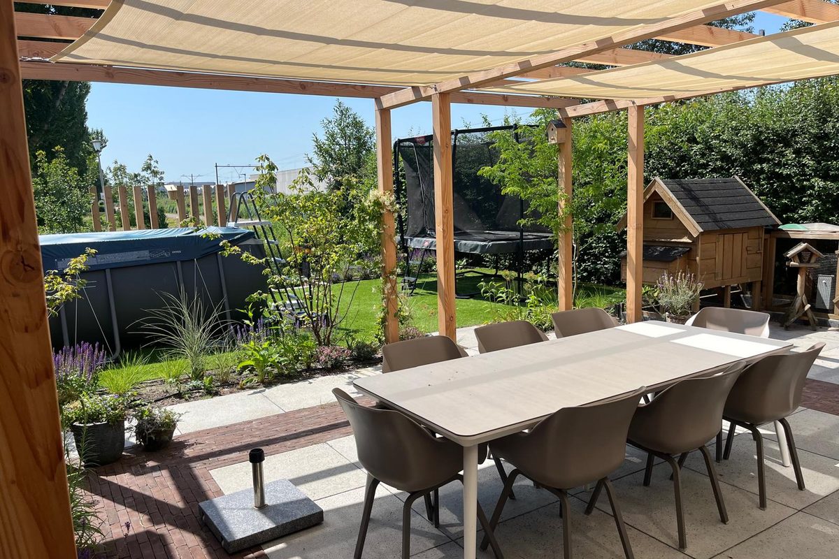 Eettafel op het terras in de schaduw van een houten pergola met schaduwdoek
