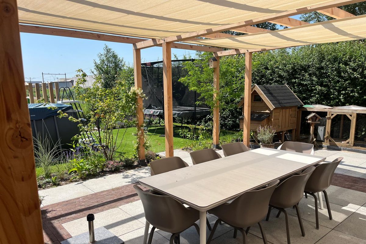 Terras met eettafel onder een pergola met schaduwdoek, met zicht op de tuin