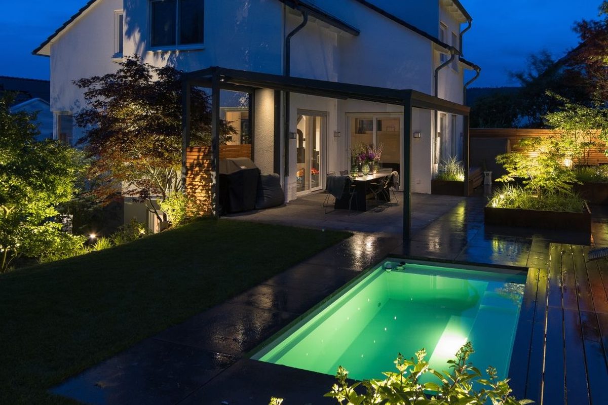 Tuin met verlicht zwembad en beplanting in de avond